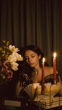 a woman sitting at a table in front of a book with two candles on it