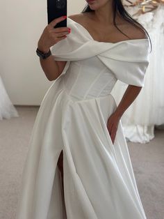 a woman in a white dress taking a selfie with her cell phone while wearing an off the shoulder gown