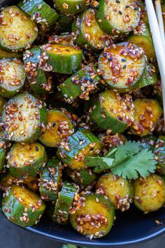 a blue bowl filled with cooked zucchini and topped with sesame seeds next to chopsticks