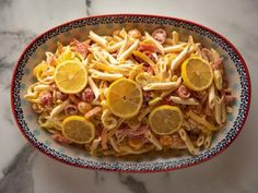 a bowl filled with pasta and lemons on top of a marble countertop,