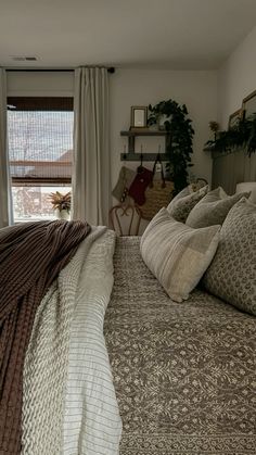 a large bed sitting in a bedroom next to a window covered in blankets and pillows