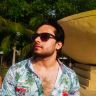 a man with sunglasses on standing in front of a fountain and looking off into the distance