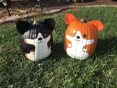 two pumpkins painted to look like dogs sitting in the grass with their faces cut out