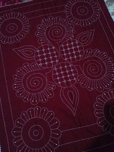 a red table cloth with an intricate design on the front and back side, sitting on a bed