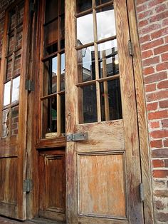 two wooden doors are open on the side of a brick building with glass panes