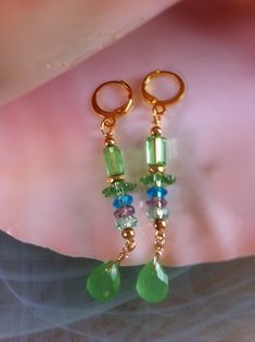 Chic and bohemian, earrings in the colors of Peridot with faceted drops of Chalcedony, Quartz pearls and Swarovski crystal. Two drops of Chalcedony faceted in Peridot green and measuring 10 mm, green, purple and aqua Quartz slices measuring 6 mm x 3 mm. Swarovski crystal in tube and Peridot-colored margarita, Gold-plated pearls and Gold-plated hoop earrings. These earrings are 6cm 5mm or 2 1/2 inches long from the top of the hook to the bottom. Peridot Color, Peridot Green, Bohemian Earrings, Swarovski Crystal, Favorite Jewelry, Jewelry Earrings Dangle, Swarovski Crystals, Dangle Drop Earrings, Violet