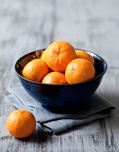 a blue bowl filled with oranges on top of a wooden table next to a napkin