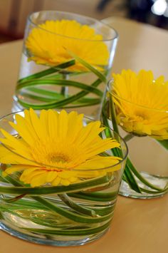 three glass vases filled with yellow flowers on top of a table