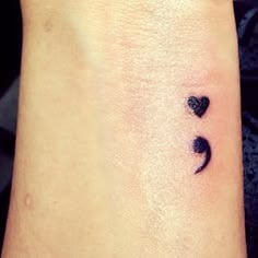 a small black heart tattoo on the left side of the wrist, with two hearts in it