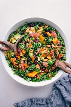 a white bowl filled with salad and wooden utensils on top of a table