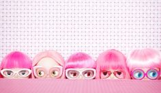 five dolls with pink hair and glasses are lined up in a row