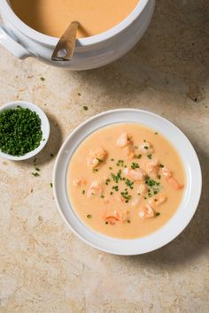 a bowl of soup next to a white bowl filled with shrimp and garnish