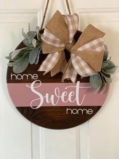 a sign that says home sweet home hanging on a door with a bow and greenery