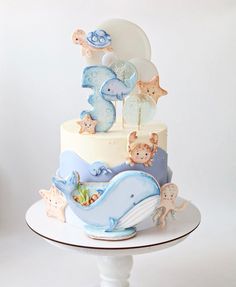 a three tiered cake decorated with blue and white fondant animals, under a cloudy sky