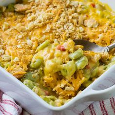 a casserole dish filled with green beans, cheese and other toppings next to a striped napkin