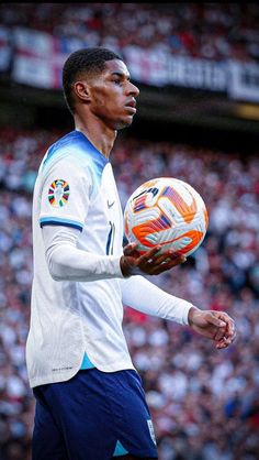 a man holding a soccer ball on top of a field in front of a crowd