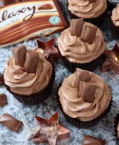 chocolate cupcakes with frosting and star decorations on a marble surface next to a bar of chocolate