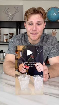 a man sitting at a table with two cups in front of him and an ad on the screen