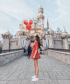 a woman in a red dress is standing on a bridge with balloons floating above her