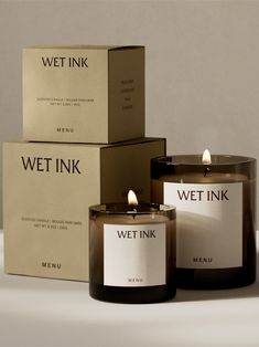 three candles sitting next to each other in front of boxes on a table with the words wet ink printed on them