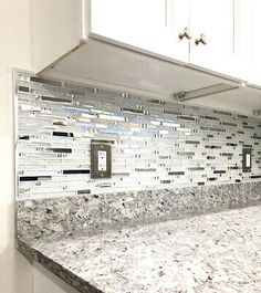 a kitchen counter top with white cabinets and marble tile backsplash in the background