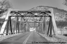 a black and white photo of a road going under a bridge with mountains in the background