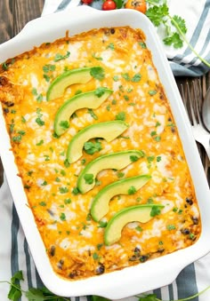 an enchilada casserole in a white dish with avocado slices on top