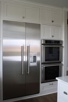 a stainless steel refrigerator and oven in a white kitchen with wood flooring, built - in cabinets and drawers