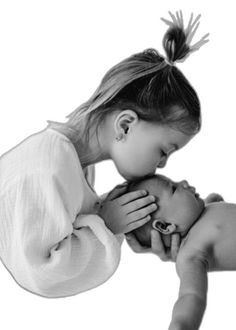 a black and white photo of a woman kissing a baby's head with her hands