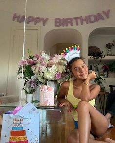 a woman sitting on the floor in front of a birthday cake with candles and flowers