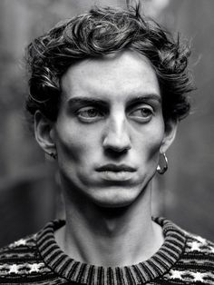 a black and white photo of a young man with curly hair wearing an earring