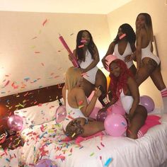 four women in white bathing suits sitting on a bed with balloons and confetti