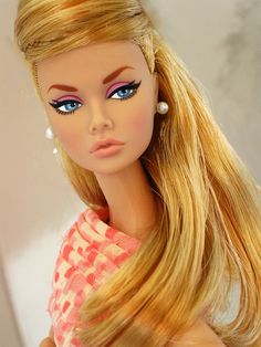 a barbie doll with long blonde hair and blue eyes wearing a pink dress in front of a white wall