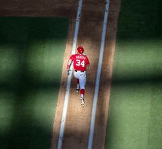 a baseball player is running to first base during a game in the sun with shadows on the ground