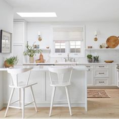 two white chairs are in the middle of a kitchen with an island and bar stools