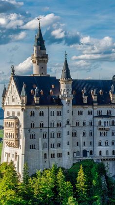 an old castle with towers and turrets on the top is surrounded by greenery, blue sky and clouds