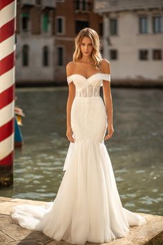 a woman in a white wedding dress standing on the edge of a body of water