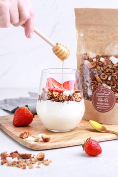 a bag of granola, yogurt and strawberries on a cutting board