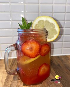 a mason jar filled with liquid and strawberries on top of a wooden table next to a lemon wedge