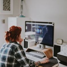 a woman sitting at a desk in front of a computer monitor with a keyboard and mouse