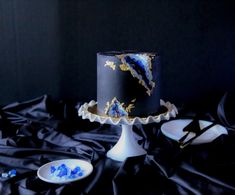 a black and gold decorated cake on a table with blue glass beads in the middle