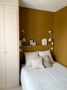 a white bed sitting in a bedroom next to a brown wall with two framed pictures on it