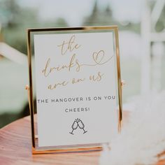 a sign that says the drinks are us on top of a wooden table with feathers