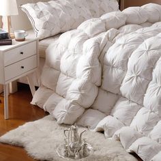 a bed with white comforter and pillows on it next to a nightstand in a bedroom