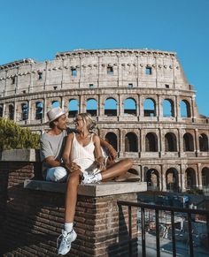 two people are sitting on a ledge in front of the colossion