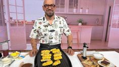 a man standing in front of a grill with corn on the cob and other foods