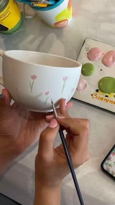 a person is painting a bowl with flowers on it and holding a pair of scissors