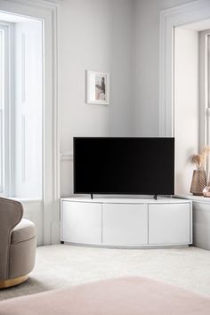 a flat screen tv sitting on top of a white entertainment center next to a window