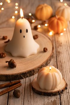 two white candles sitting on top of a wooden table next to pumpkins and cinnamon sticks