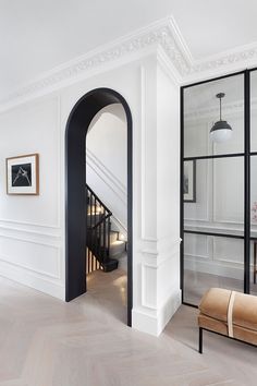 an open doorway leading to a living room with white walls and wood floors, along with a bench in the middle